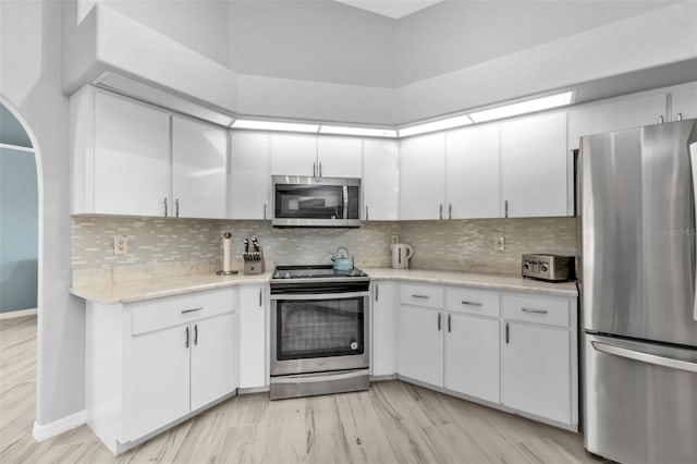 kitchen with light wood finished floors, backsplash, appliances with stainless steel finishes, white cabinets, and baseboards