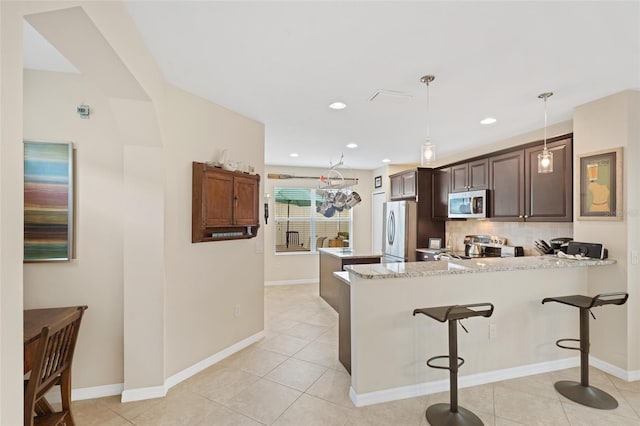 kitchen with a breakfast bar, light tile patterned floors, decorative backsplash, appliances with stainless steel finishes, and a peninsula