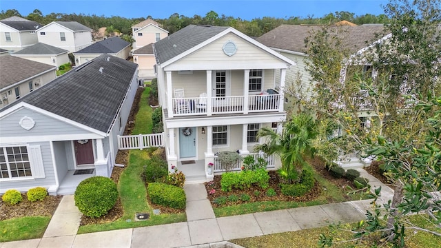 neoclassical home featuring a balcony, a residential view, roof with shingles, fence, and a porch