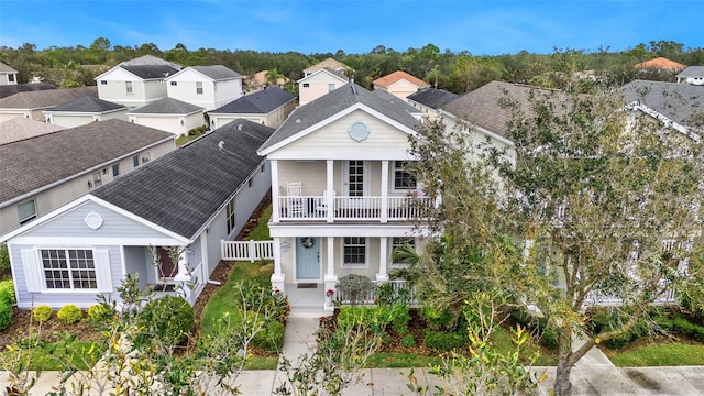 view of front facade with a balcony, a residential view, roof with shingles, fence, and a porch