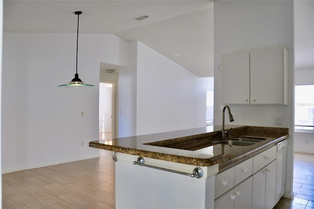 kitchen with decorative light fixtures, lofted ceiling, white cabinetry, a sink, and dark stone counters