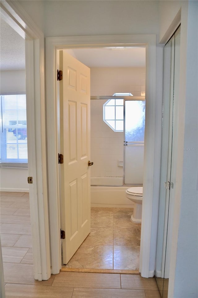 bathroom featuring shower / bath combination with glass door, plenty of natural light, and toilet