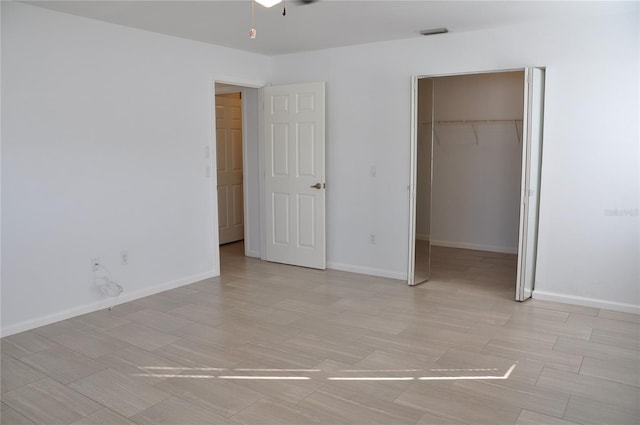 unfurnished bedroom featuring a closet, a walk in closet, visible vents, and baseboards