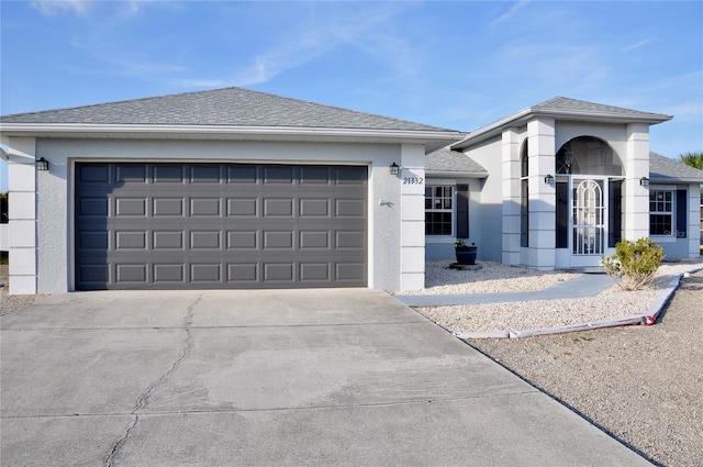 view of front facade featuring a shingled roof, driveway, an attached garage, and stucco siding