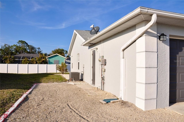 view of side of property with a garage, central AC, fence, and stucco siding