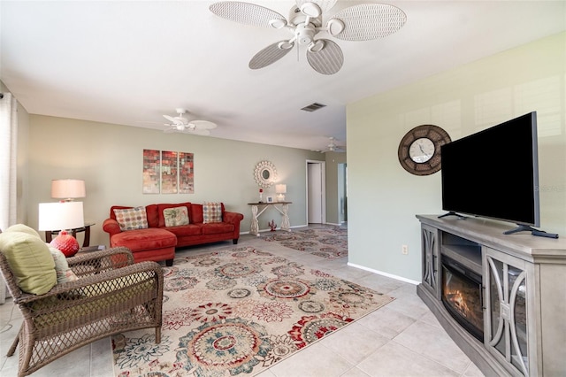 living area with light tile patterned floors, visible vents, a glass covered fireplace, ceiling fan, and baseboards