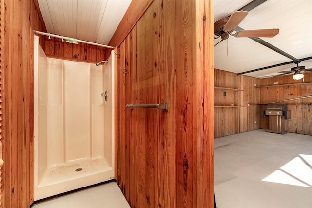 bathroom with a ceiling fan, wooden walls, and a shower stall