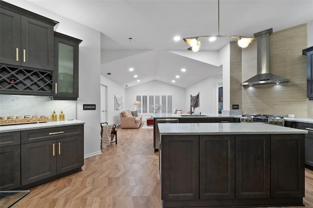 kitchen featuring open floor plan, hanging light fixtures, vaulted ceiling, wall chimney exhaust hood, and glass insert cabinets