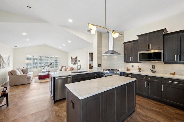 kitchen featuring appliances with stainless steel finishes, open floor plan, a peninsula, wall chimney range hood, and a sink