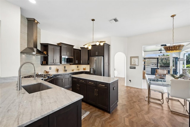 kitchen with range hood, arched walkways, decorative light fixtures, appliances with stainless steel finishes, and a sink