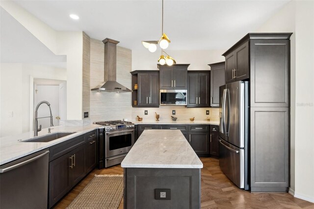 kitchen with stainless steel appliances, a sink, wall chimney range hood, light stone countertops, and decorative light fixtures