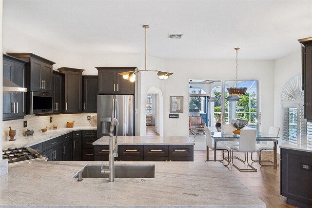 kitchen with tasteful backsplash, visible vents, hanging light fixtures, stainless steel refrigerator with ice dispenser, and a sink