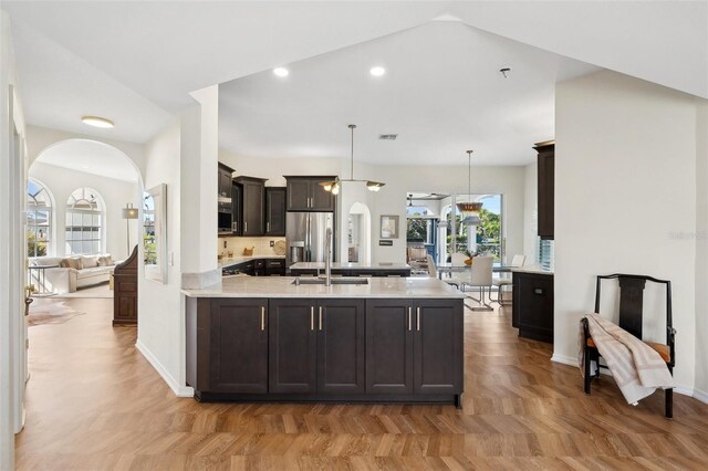 kitchen with dark brown cabinetry, a peninsula, a sink, hanging light fixtures, and stainless steel fridge