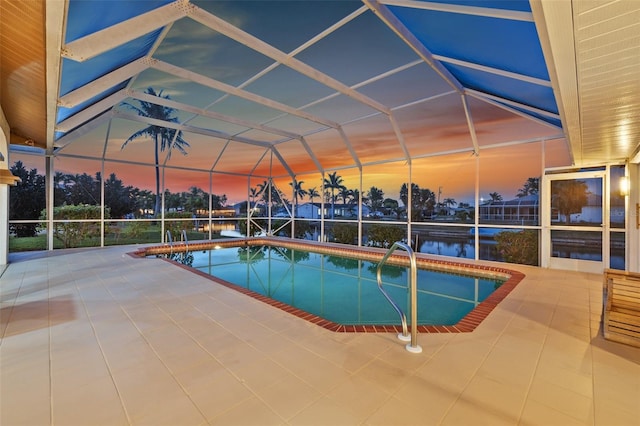 pool at dusk featuring a water view, a patio area, a lanai, and an outdoor pool