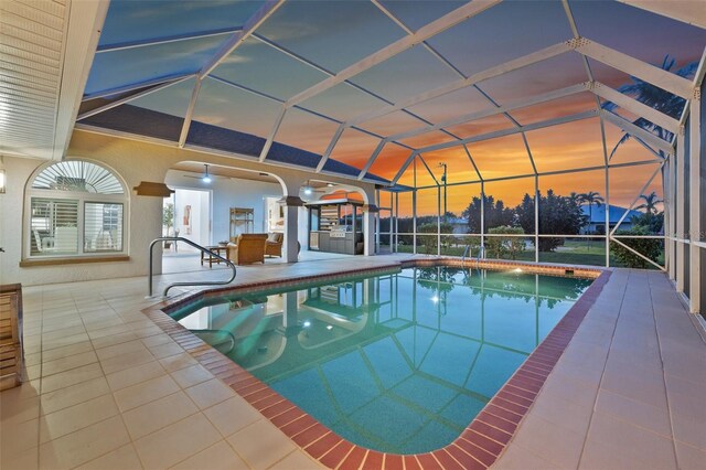 outdoor pool with glass enclosure, a patio area, and a ceiling fan