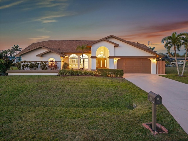 view of front facade with a garage, a lawn, driveway, and stucco siding