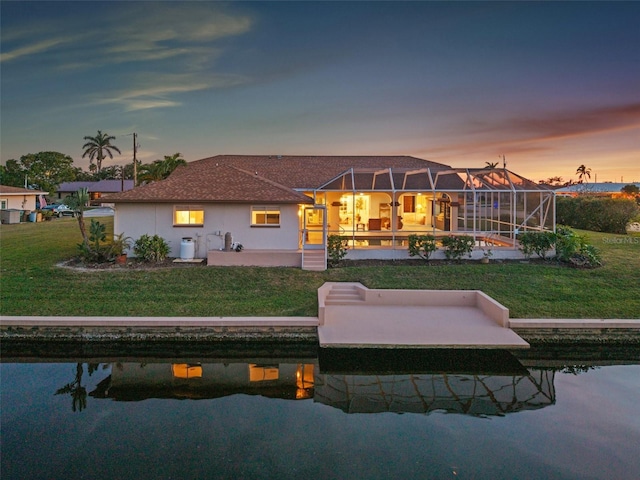 back of property at dusk with glass enclosure, stucco siding, a patio, and a yard