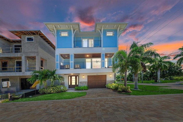 view of front of property with a garage, a balcony, stone siding, decorative driveway, and stucco siding