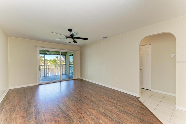 unfurnished room with arched walkways, visible vents, a ceiling fan, wood finished floors, and baseboards