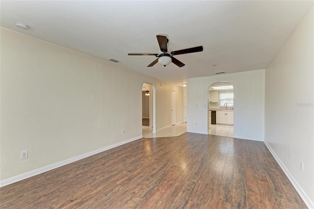 unfurnished living room with baseboards, arched walkways, a ceiling fan, wood finished floors, and a sink