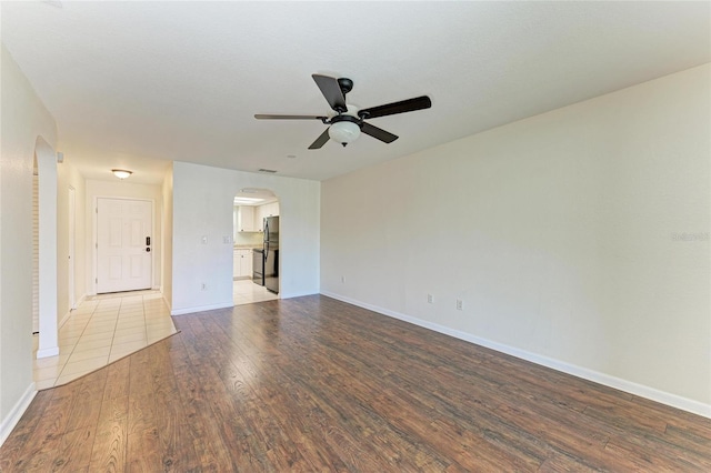 spare room with arched walkways, ceiling fan, baseboards, and wood finished floors