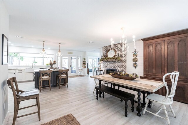 dining room with a chandelier, a brick fireplace, visible vents, and light wood finished floors