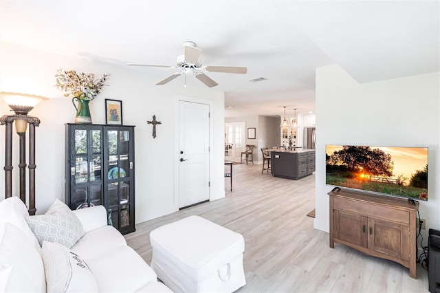 living area featuring light wood-type flooring, visible vents, ceiling fan, and baseboards