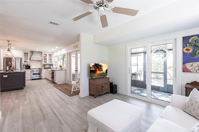 living area with a healthy amount of sunlight, light wood-type flooring, visible vents, and baseboards