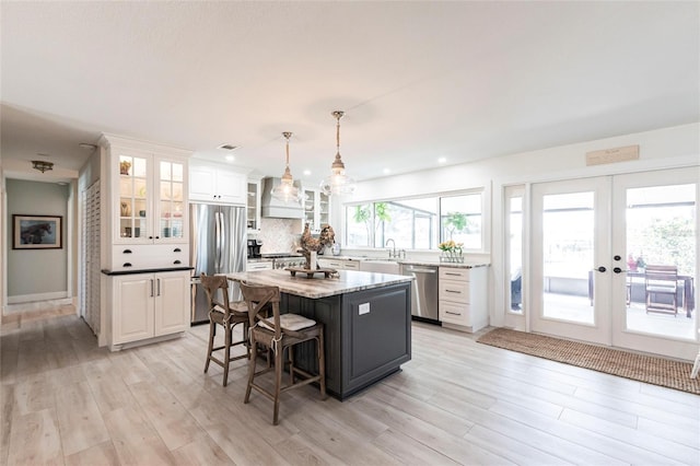 kitchen featuring a kitchen island, glass insert cabinets, appliances with stainless steel finishes, decorative light fixtures, and white cabinetry