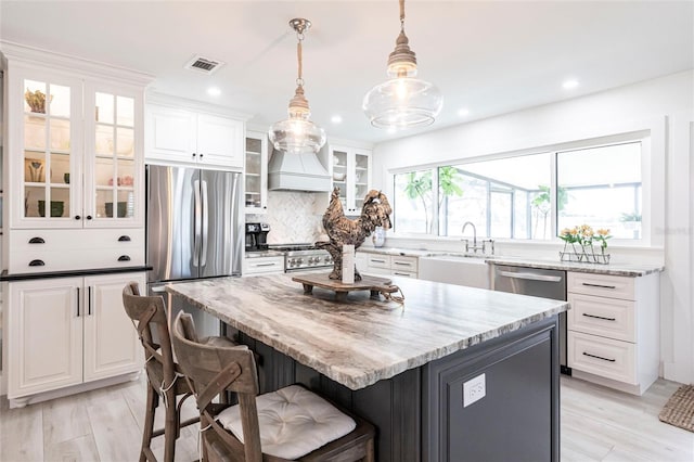 kitchen with hanging light fixtures, a kitchen island, visible vents, and white cabinets