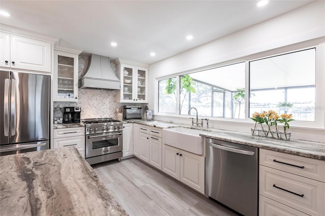 kitchen featuring glass insert cabinets, custom range hood, appliances with stainless steel finishes, and white cabinets