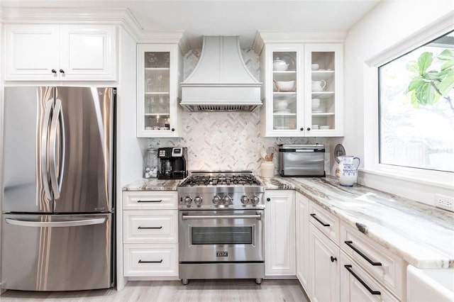 kitchen featuring white cabinetry, custom range hood, glass insert cabinets, and stainless steel appliances