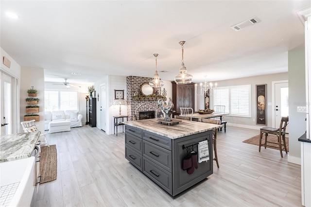 kitchen featuring visible vents, light stone counters, open floor plan, gray cabinetry, and pendant lighting