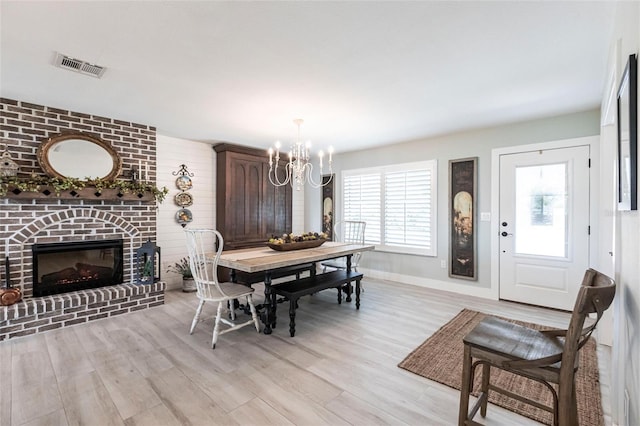 dining space featuring a chandelier, a fireplace, visible vents, baseboards, and light wood finished floors