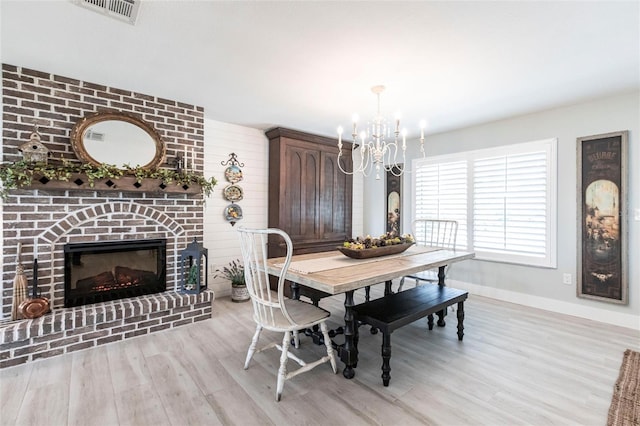 dining space featuring baseboards, visible vents, an inviting chandelier, light wood-type flooring, and a brick fireplace