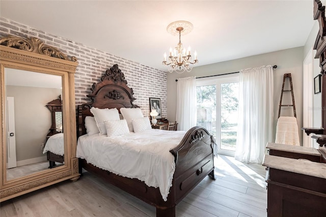 bedroom featuring access to exterior, light wood-style flooring, brick wall, and an inviting chandelier