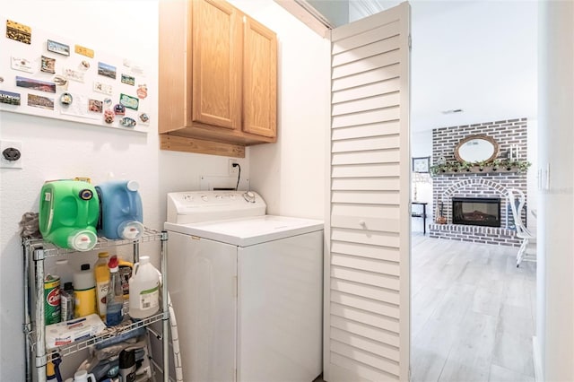 laundry room with cabinet space, a fireplace, washer / clothes dryer, and light wood finished floors