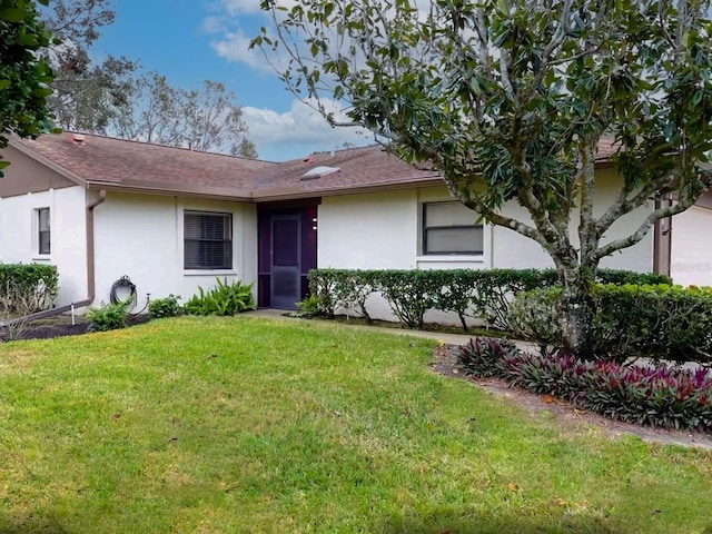 ranch-style house featuring a front yard, roof with shingles, and stucco siding