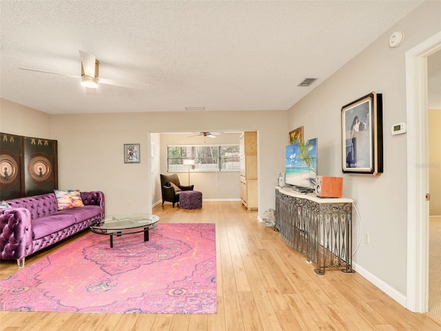 living area featuring a textured ceiling, wood finished floors, visible vents, baseboards, and a ceiling fan