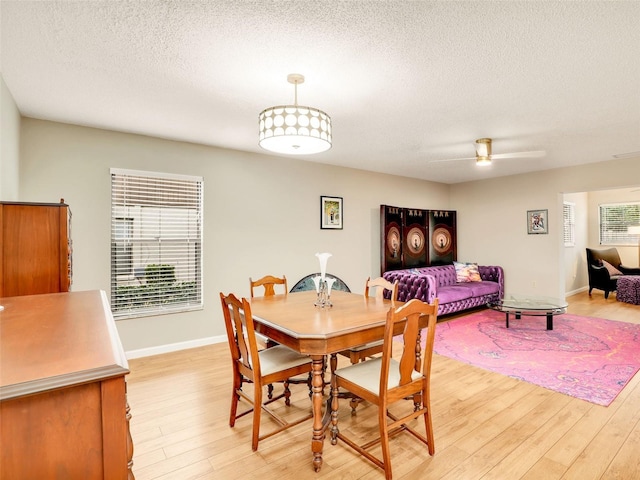 dining area featuring a textured ceiling, baseboards, a ceiling fan, and light wood-style floors