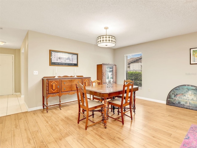 dining space with light wood-style floors, a textured ceiling, and baseboards