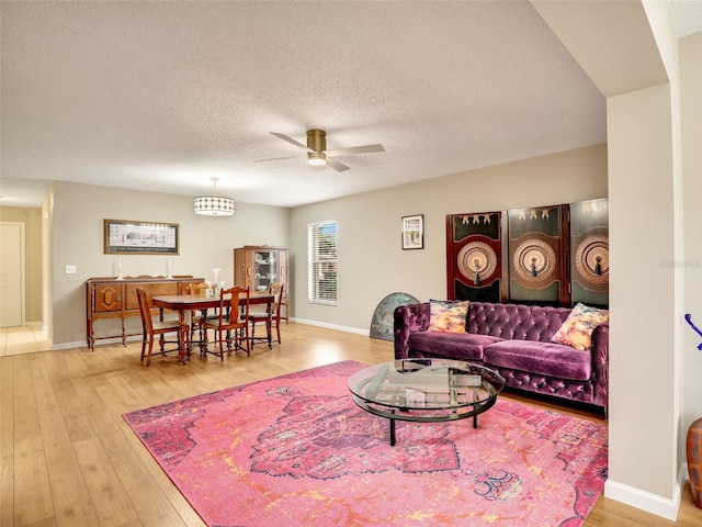 living area featuring a textured ceiling, wood finished floors, a ceiling fan, and baseboards