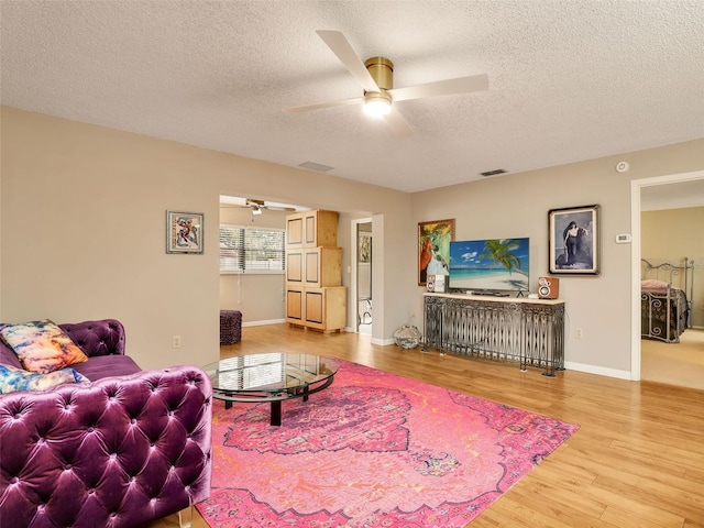 living room with baseboards, visible vents, a ceiling fan, wood finished floors, and a textured ceiling