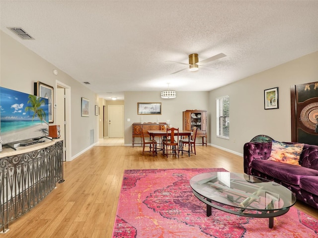 living room with visible vents, light wood-style floors, a ceiling fan, a textured ceiling, and baseboards