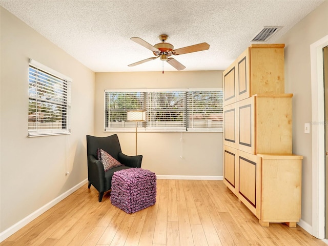 living area featuring light wood finished floors, baseboards, visible vents, and ceiling fan