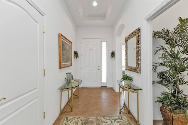 entrance foyer with light tile patterned floors, baseboards, arched walkways, a raised ceiling, and crown molding