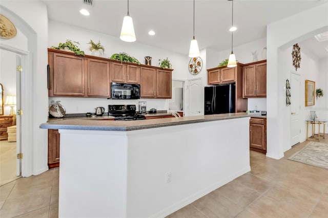 kitchen with dark countertops, brown cabinets, hanging light fixtures, a kitchen island with sink, and black appliances