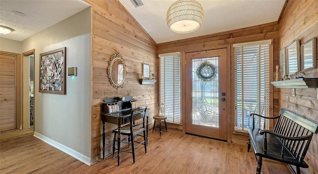 entrance foyer with lofted ceiling, plenty of natural light, light wood-style flooring, and wooden walls