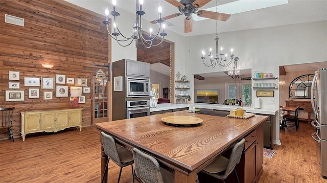 kitchen featuring wooden walls, a peninsula, stainless steel appliances, light countertops, and light wood finished floors