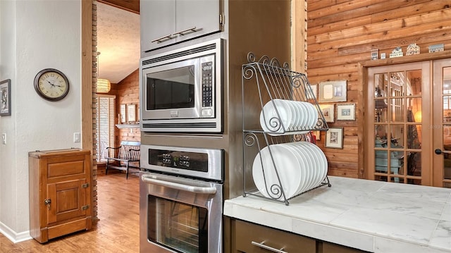 kitchen featuring lofted ceiling, light wood finished floors, appliances with stainless steel finishes, and tile counters